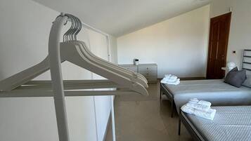 Ein Hotelzimmer mit zwei Betten, einem weißen Kleiderhaken, einem kleinen Tisch mit Lampe und einer Tür im Hintergrund.