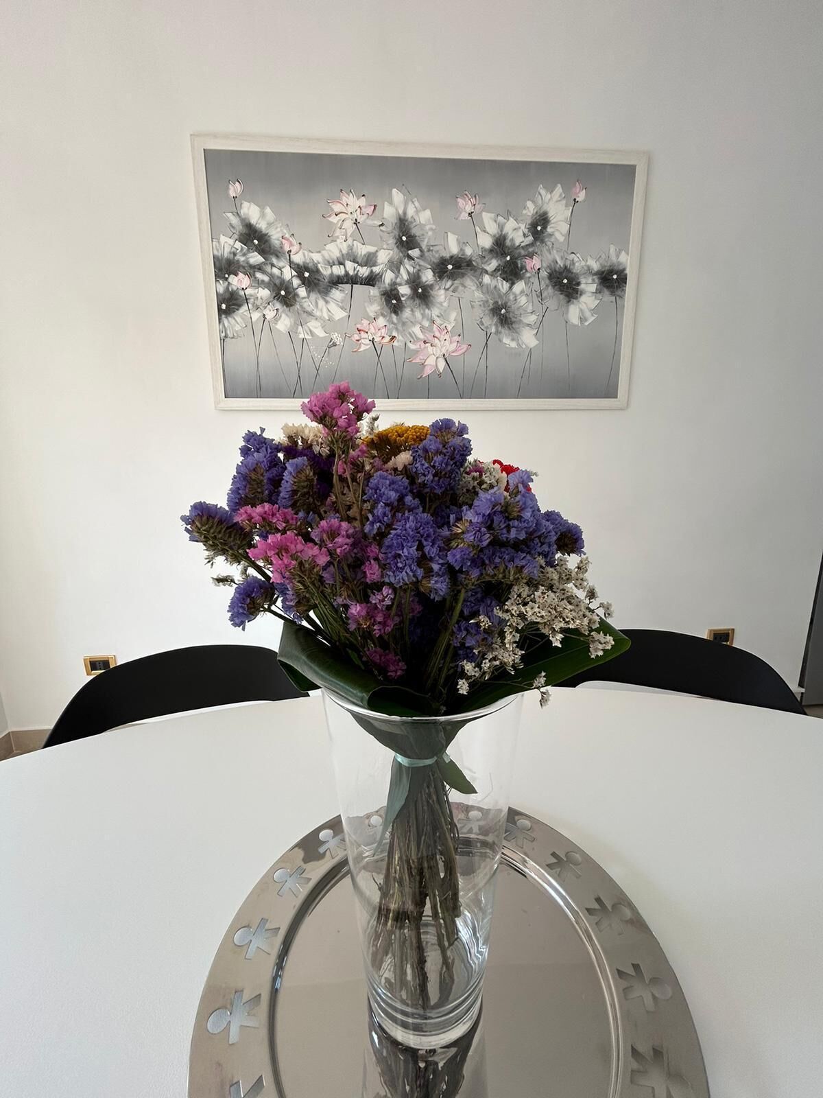Un vase en verre transparent contenant un bouquet de fleurs, posé sur une table ronde en verre.