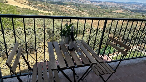 Ein Balkon mit Holztisch und -stühlen, einem Blumentopf und einer Weinflasche.