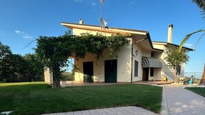 Ein Haus mit einer gefliesten Terrasse, die ein Kompassmuster zeigt, einem Garten und einem strahlend blauen Himmel.