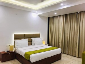 A modern hotel room with a large bed, a nightstand, a bedside lamp, and a window with curtains. - Hotels Vibes  (Vikasnagar)