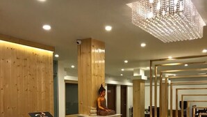 A modern reception area with a wooden reception desk, a Buddha statue, and a geometric light fixture. - Hotels Vibes  (Vikasnagar)