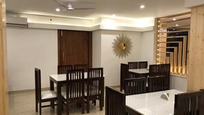 A dining area with wooden chairs and tables, a ceiling fan, recessed lighting, and a decorative wall piece. - Hotels Vibes  (Vikasnagar)