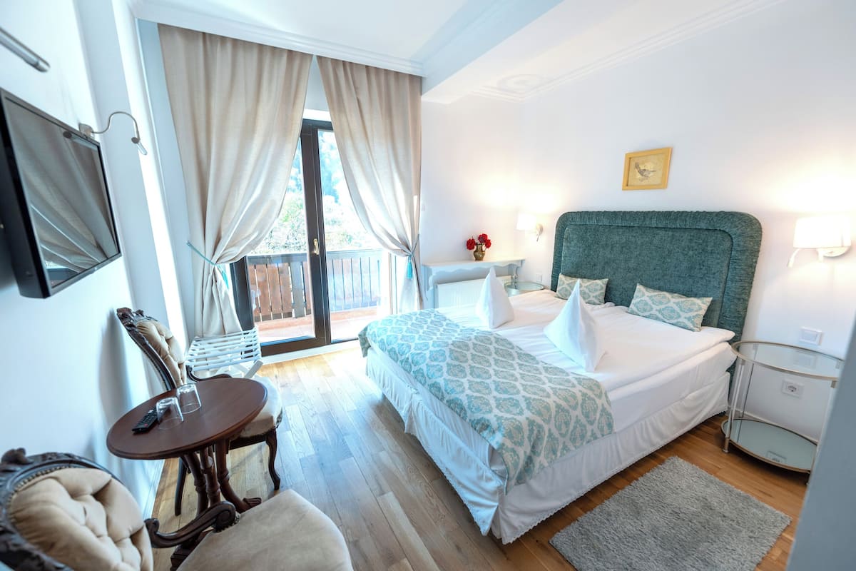 Una camera da letto con un letto, un comodino, una sedia, un tavolino con un telecomando e una finestra con tende.