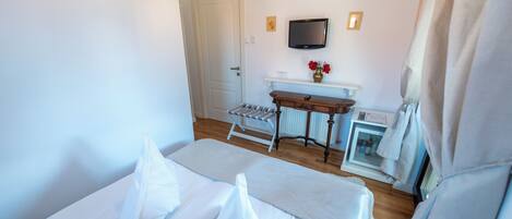 A hotel room with a bed, a small table with a vase of flowers, a television mounted on the wall, and a radiator.
