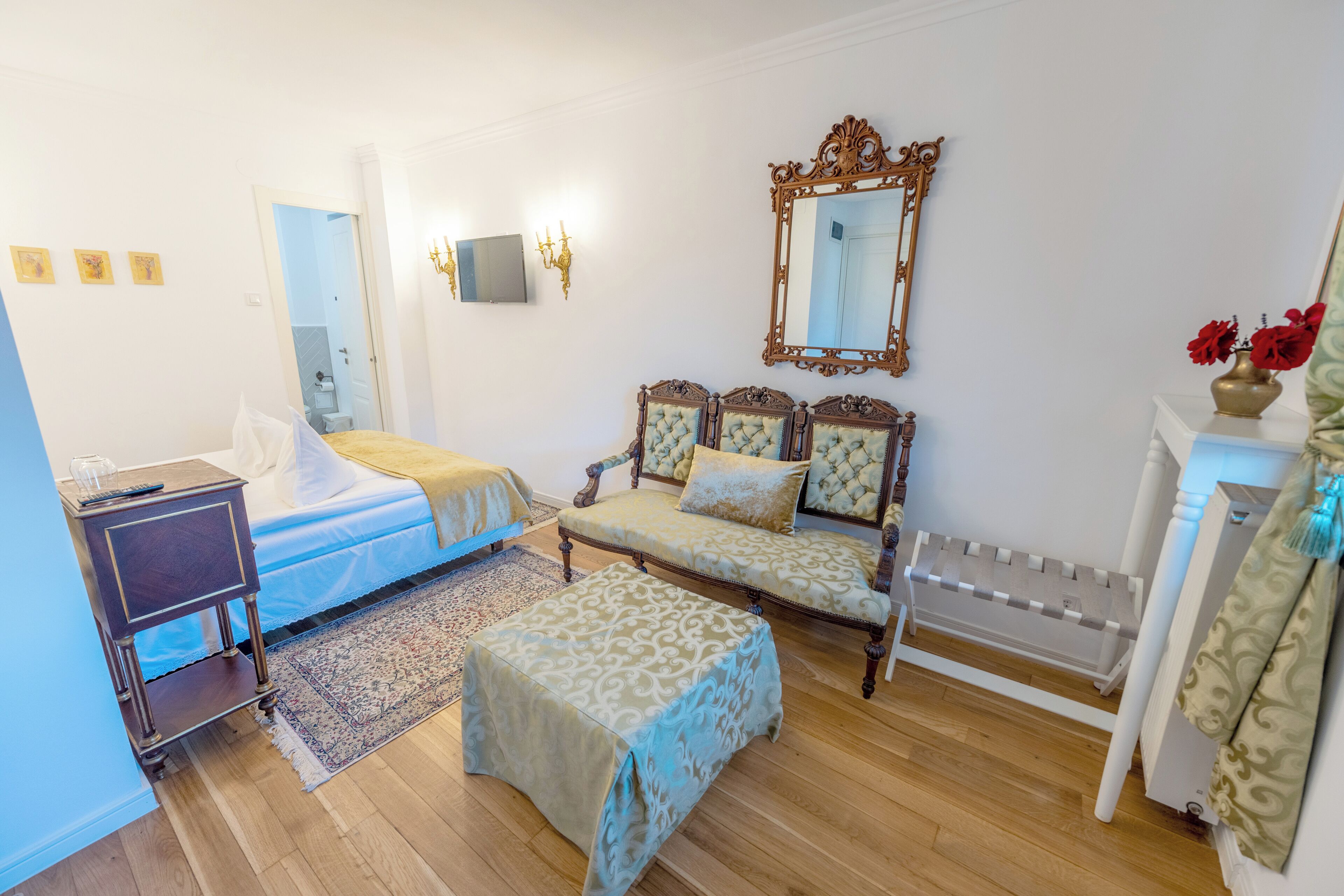 A bedroom with a bed, bedside table, nightstand, dresser, mirror, and a small table with a vase.