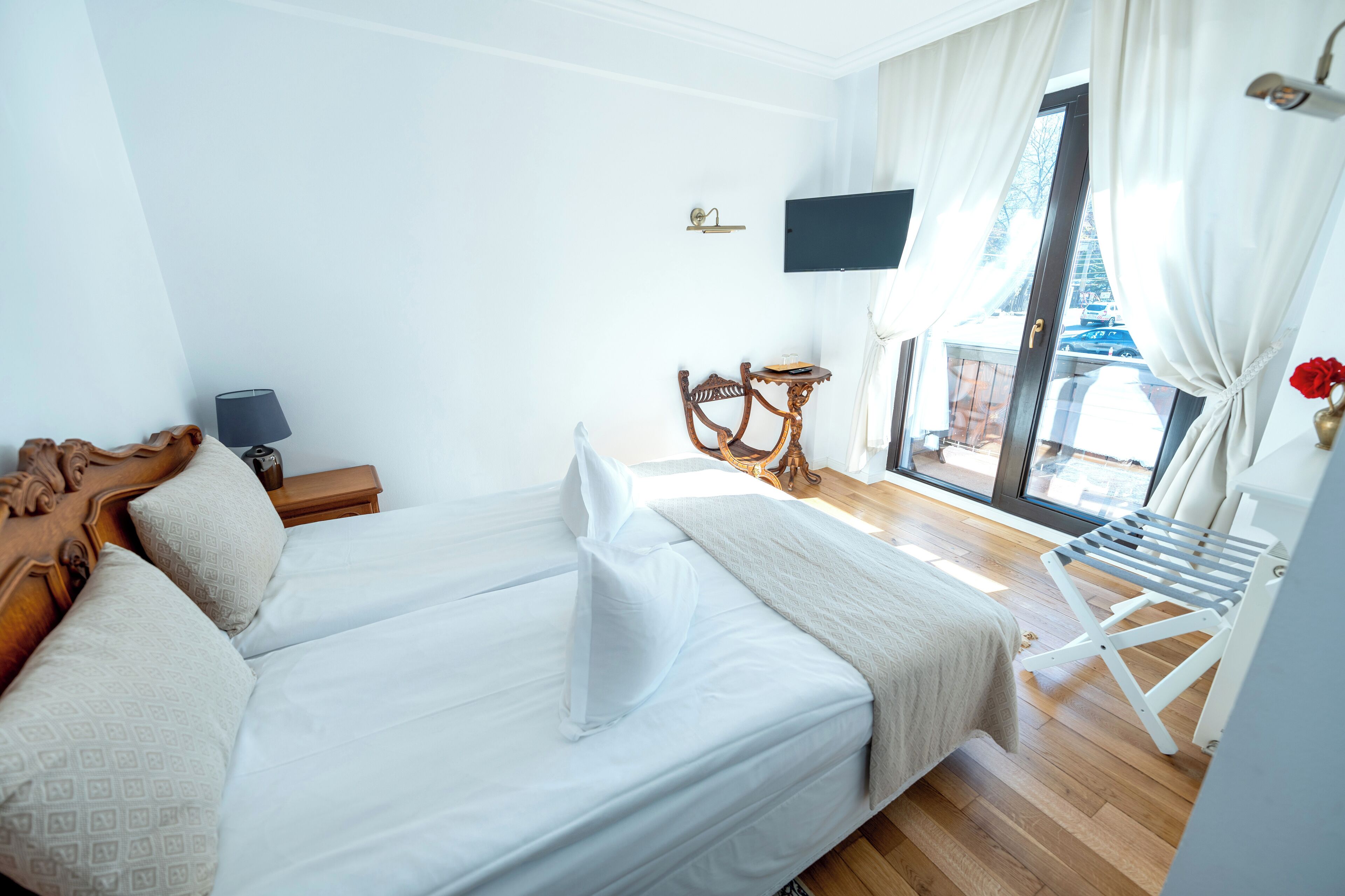 A hotel room with a bed, a small table with a lamp, a chair, and a TV on the wall.