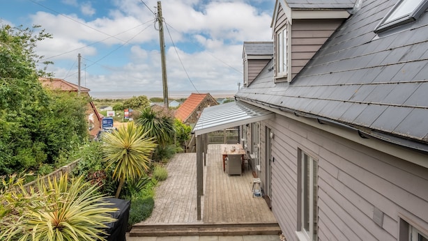 Um imóvel residencial com deck de madeira, área de estar coberta ao ar livre e vista para o mar.