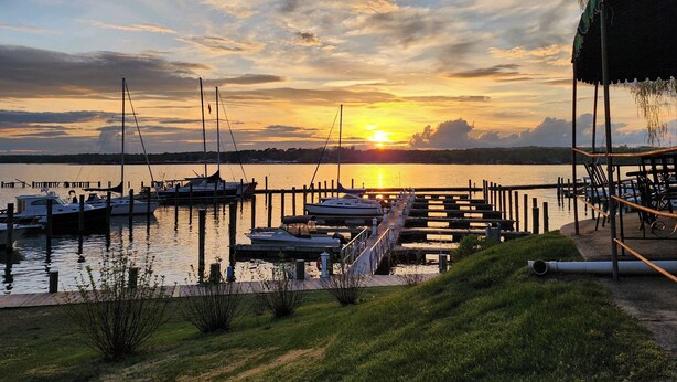 Un port de plaisance avec des bateaux amarrés, une jetée s’avançant dans l’eau et une zone herbeuse dotée d’un espace de repos abrité.