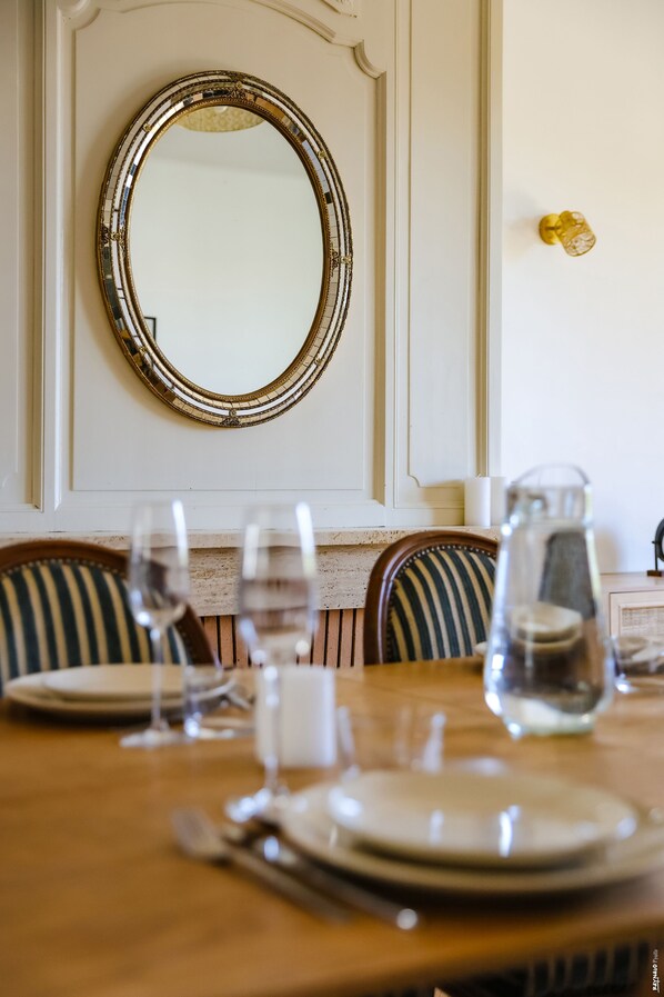 A dining table set with plates, glasses, and cutlery, a striped chair, and a decorative mirror on the wall.