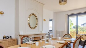 A dining area with a wooden table set for six, surrounded by striped upholstered chairs. A large mirror hangs above the table, and a fireplace is visible in the background.