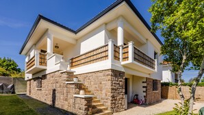 A two-story house with a stone facade, a balcony with wooden railings, and a clear blue sky.