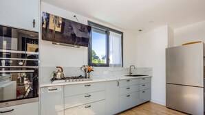 A modern kitchen with a built-in oven, a stainless steel refrigerator, and a window with curtains.