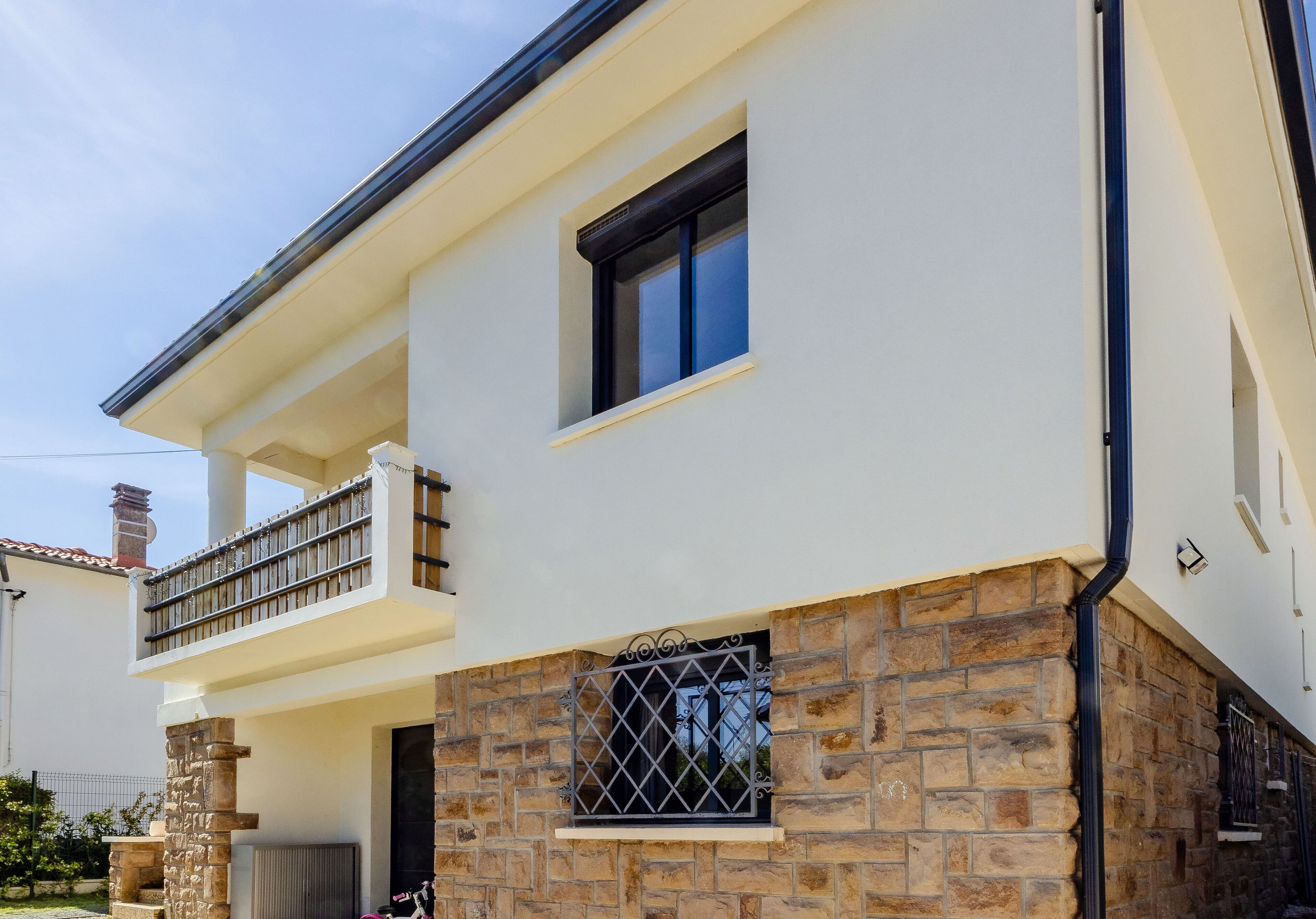 A two-story building with a balcony, stone facade, and a window with metal bars.