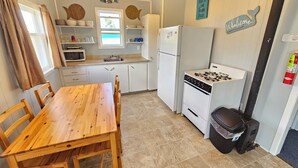 A compact kitchen with white cabinets, a wooden dining table, and a stove. - Lyons Cottages - Cottage #5, 2BR Walk to the Beaches of Stanhope National Park! (Stanhope)