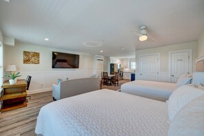 A hotel room with two beds, a desk with a lamp, a chair, a dining table, and a TV on the wall.