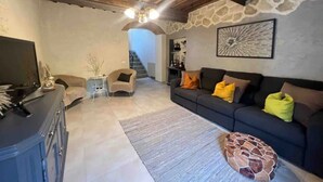 A living room with a stone wall, a sofa with orange pillows, a coffee table, and a TV on a cabinet.
