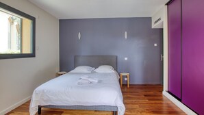 Ein Schlafzimmer mit einem Bett, Holzboden, einem Fenster und einem lila Kleiderschrank.