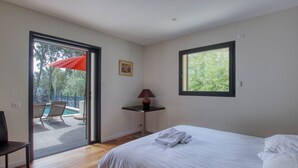 Ein Schlafzimmer mit einem Bett, einem Fenster, einer Tür, die auf einen Balkon führt, und einem kleinen Tisch mit einer Lampe.