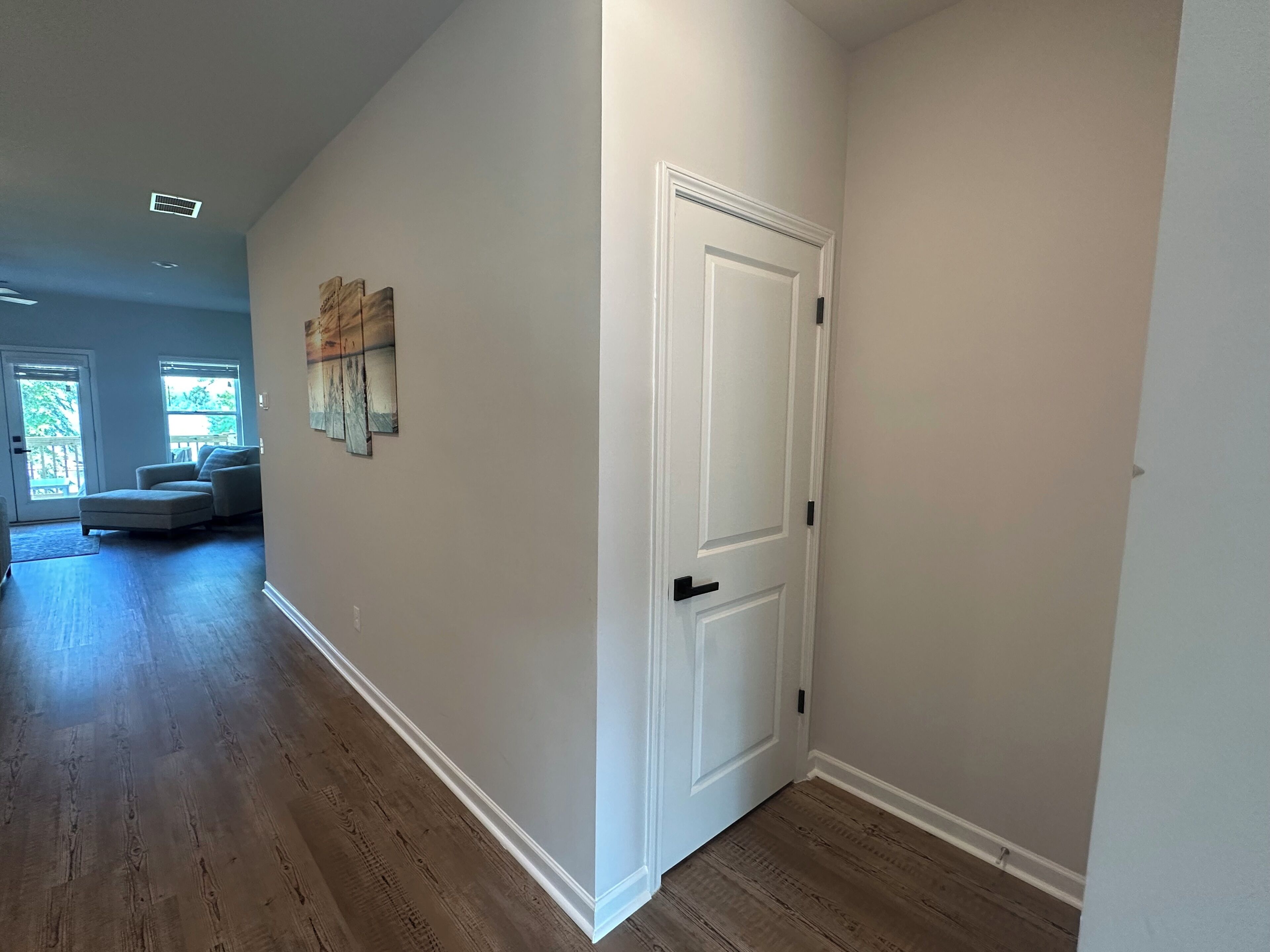 A hallway with a white door, wooden flooring, and a painting on the wall.