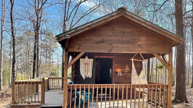 A wooden cabin with a porch, steps leading up to the entrance, and a small table and chair outside. - Cozy cabin and contemporary container home on one property! Pets welcome! (Enoree)