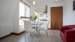 Een moderne keuken met witte kastjes, een houten deur en een eethoek met een glazen tafel en witte stoelen.