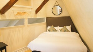 Een slaapkamer met een bed, houten balken, een spiegel en een houten vloer.