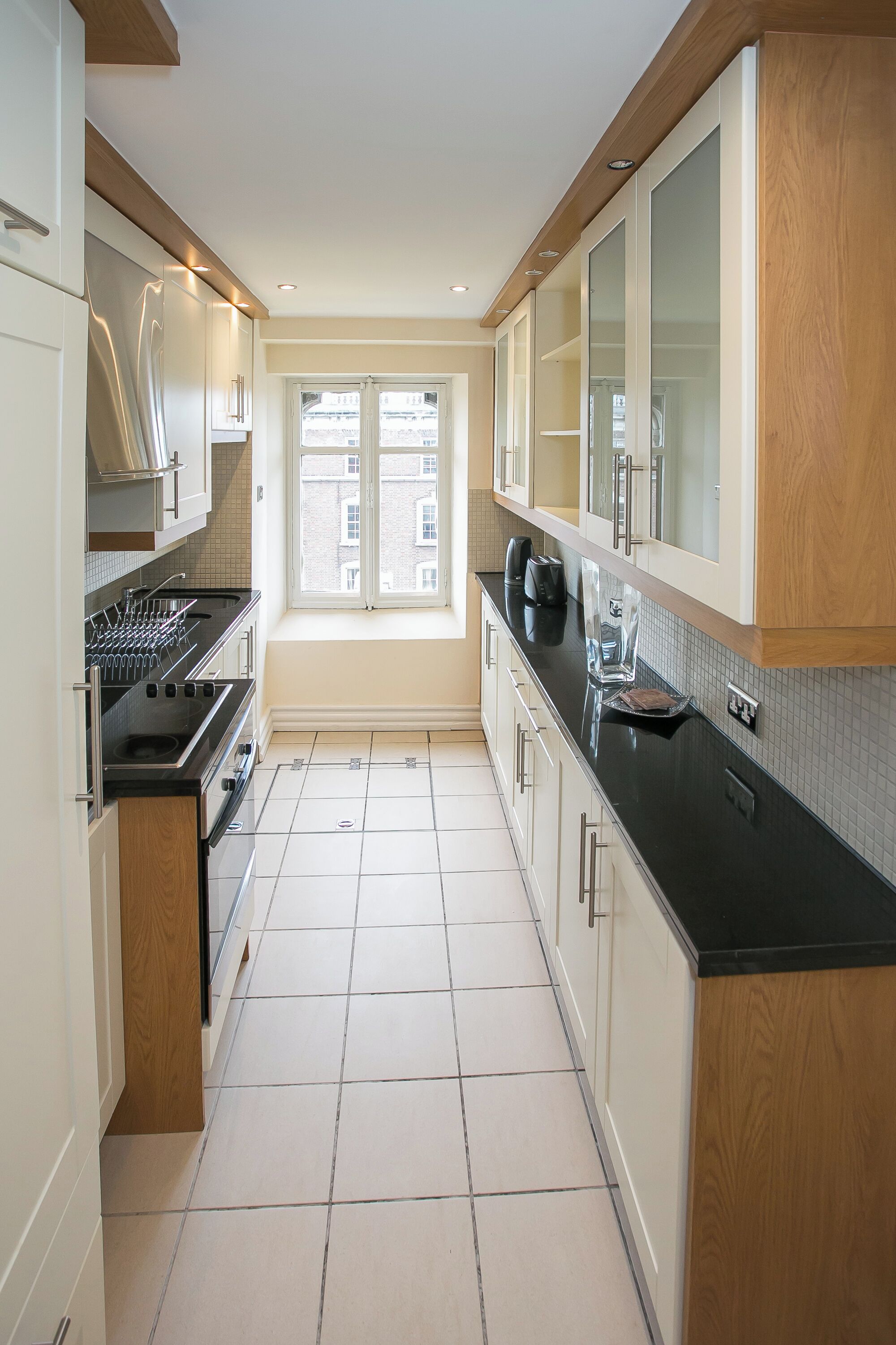 A narrow kitchen with white cabinets, a black countertop, and a window providing natural light.