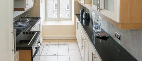 A narrow kitchen with white cabinets, a black countertop, and a window providing natural light.