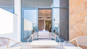 A modern hotel room with a large glass door leading to a balcony with two wicker chairs.