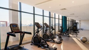 A modern gym with multiple cardio machines, large windows, and a view of the city.