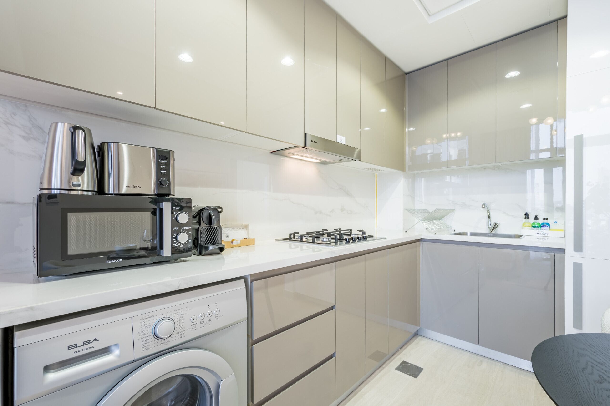 A modern kitchen with a built-in washing machine, a microwave, a coffee maker, and a gas stove.