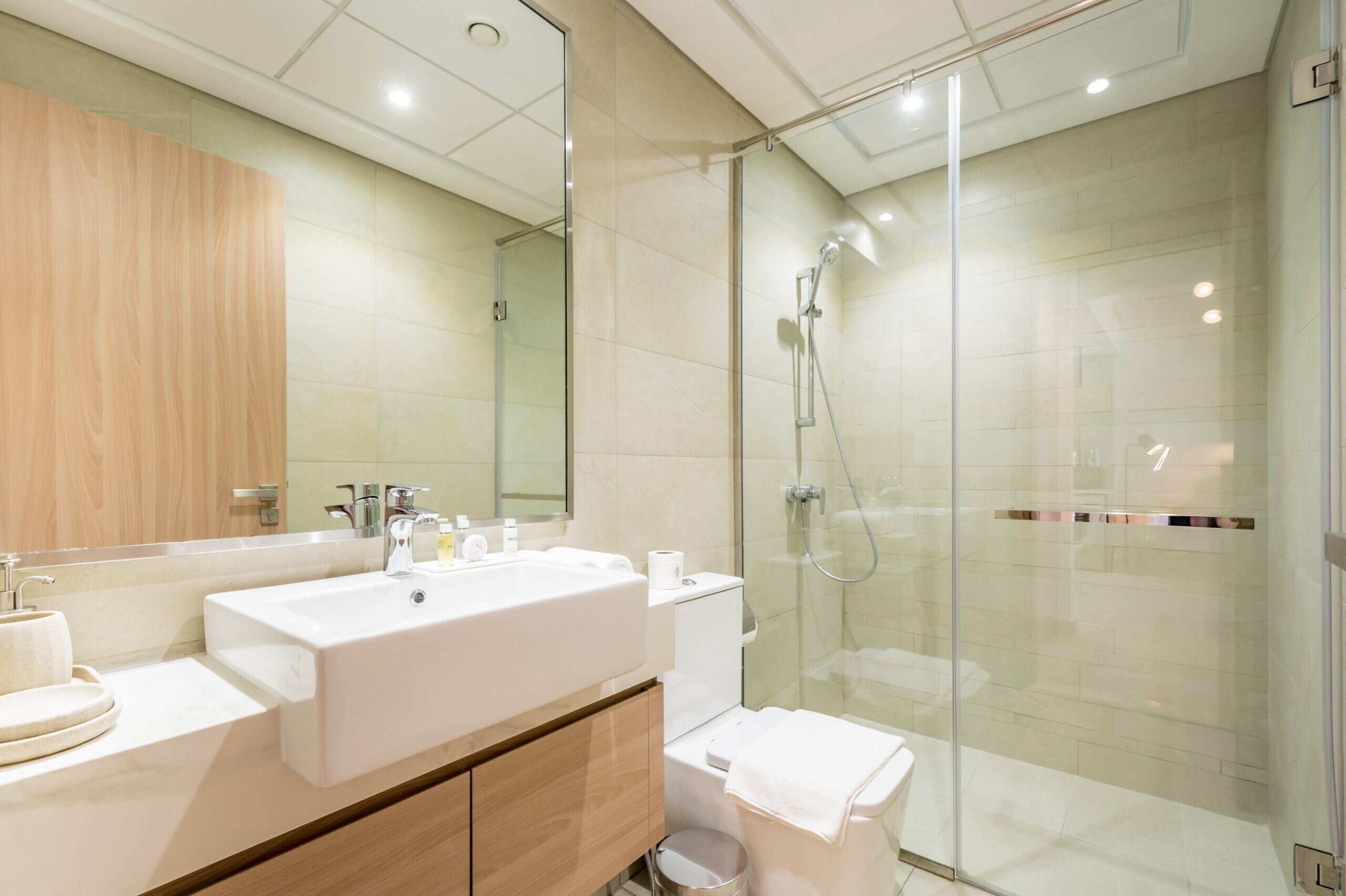 Un baño moderno con cabina de ducha acristalada, un espejo grande y un lavabo blanco.