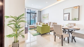 A modern living room with a sofa, dining table, and chairs. There is a large mirror on the wall and a potted plant. - Cosmopolitan 1BR Apartment in Celestia B, Dubai South by Deluxe Holiday Homes (Dubai)