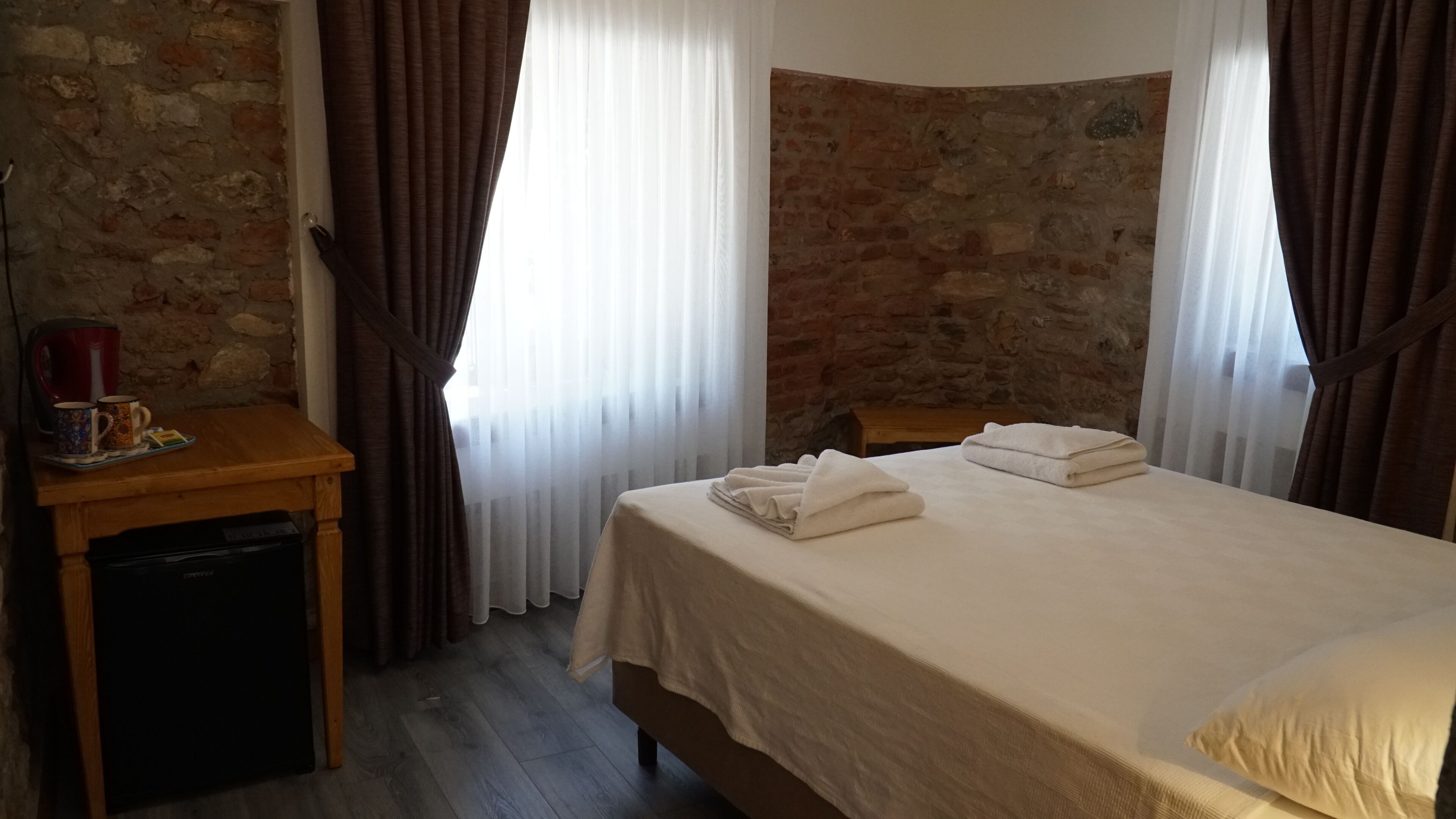Quarto de hotel com cama, escrivaninha de madeira, chaleira e uma xícara.