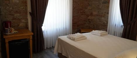 Quarto de hotel com cama, escrivaninha de madeira, chaleira e uma xícara.