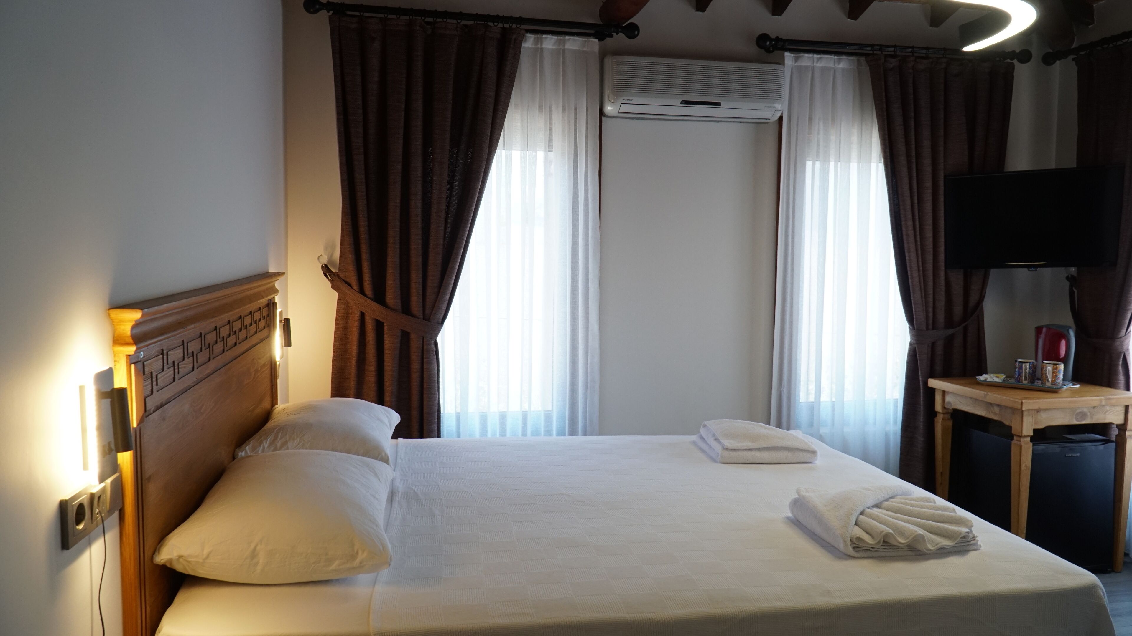 A hotel room with a bed, curtains, an air conditioning unit, a television, and a small table with a tray.