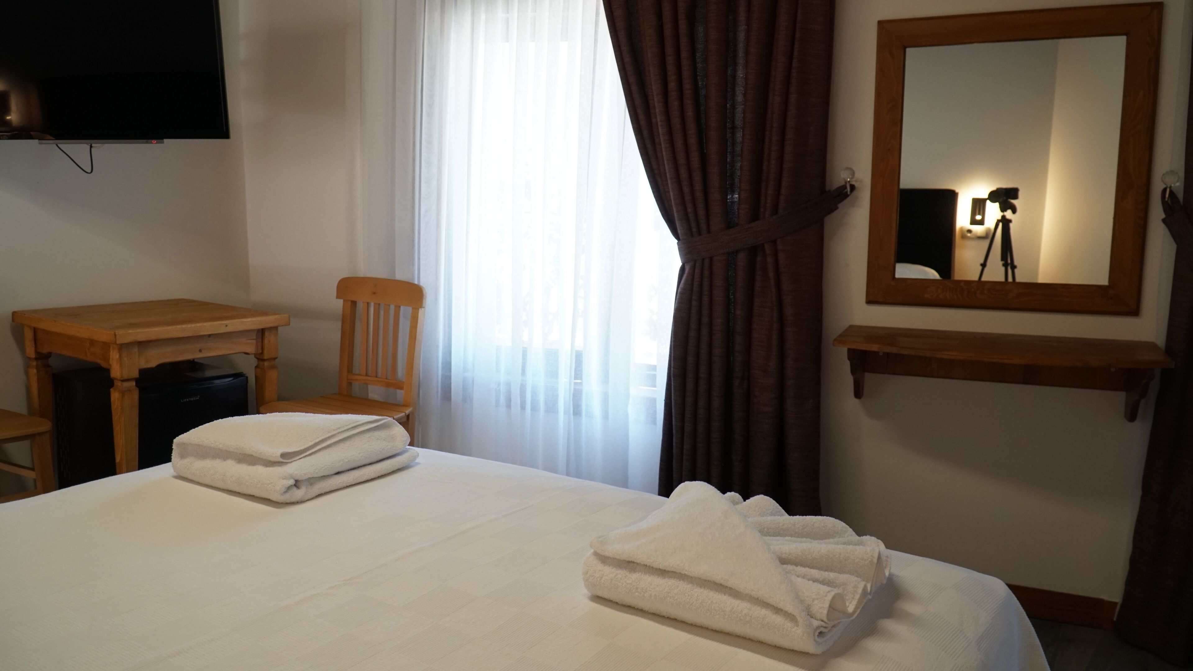 Une chambre d’hôtel équipée d’un lit, d’un bureau, d’une chaise, d’une télévision, d’un miroir et d’une fenêtre avec des rideaux.