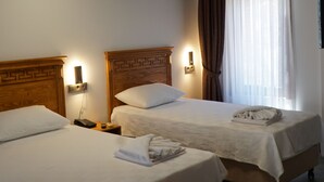 Camera d'albergo con due letti, poggiatesta in legno, lampade sui comodini, una panca e condizionatore a soffitto.