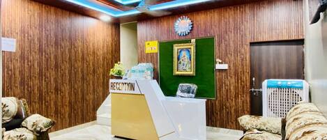 A reception area with a reception desk, wooden panel walls, a clock, and a green wall with a framed picture.