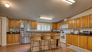 A modern kitchen with wooden cabinets, a stainless steel refrigerator, a microwave, and a toaster. There are three wicker bar stools and a wooden countertop. - Trout House, Trout House 4bd/3ba on the South Holston River (Bristol)