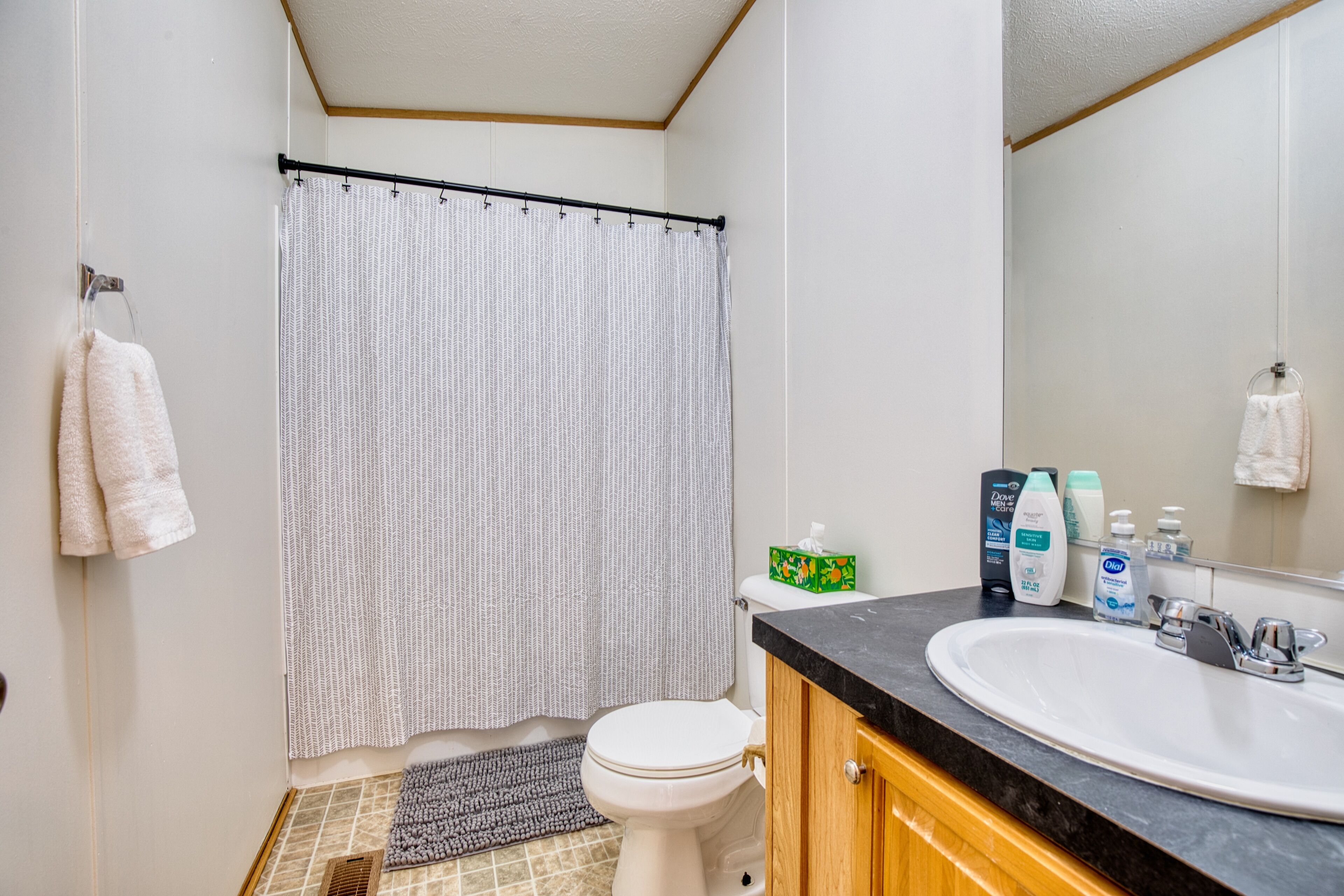 A bathroom with a toilet, sink, and shower curtain. There are toiletries on the sink counter.