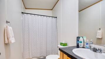 A bathroom with a toilet, sink, and shower curtain. There are toiletries on the sink counter.