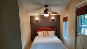 Ein Schlafzimmer mit einem Bett, einem Deckenventilator und einem Fenster mit Jalousien.