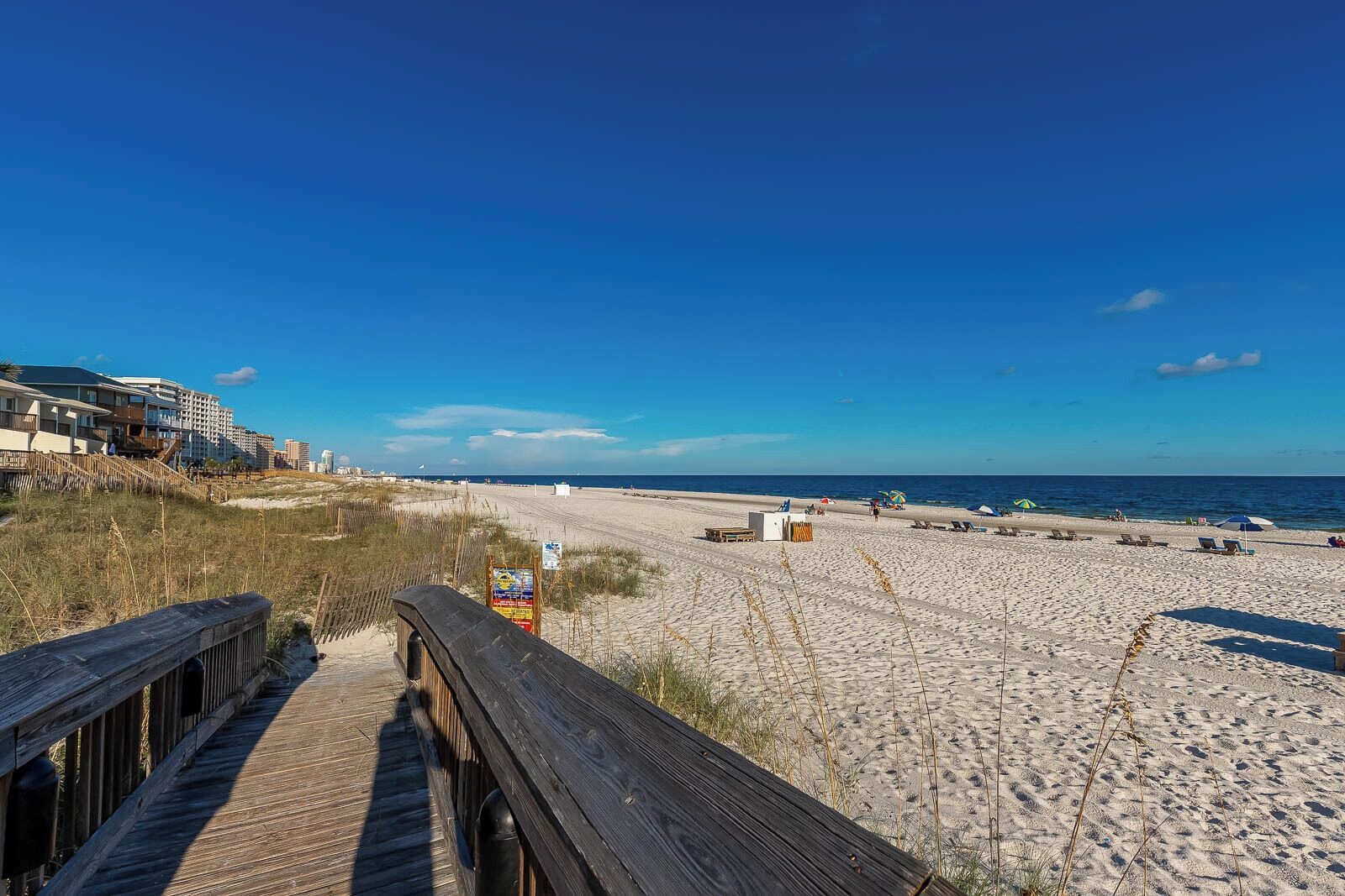 Een strand met een houten looppad dat naar een gebouw met meerdere verdiepingen leidt.