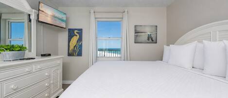 Une chambre avec un grand lit, un ventilateur de plafond, une commode, un téléviseur et une vue sur la plage.