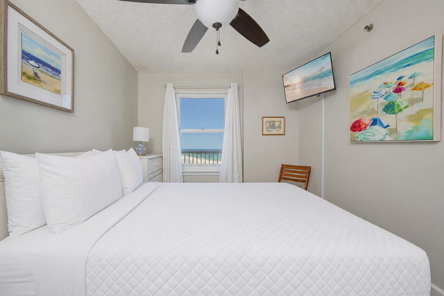 Ein Hotelzimmer mit Bett, Deckenventilator, Fernseher und Blick auf den Strand.