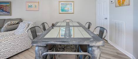 Een eetgedeelte met een tafel met glazen blad, metalen stoelen, een geborduurde plaid en kunstwerken aan de muur.