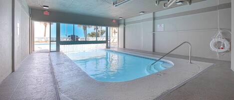 An indoor swimming pool with clear glass walls, a lifebuoy, and a visible exit sign.