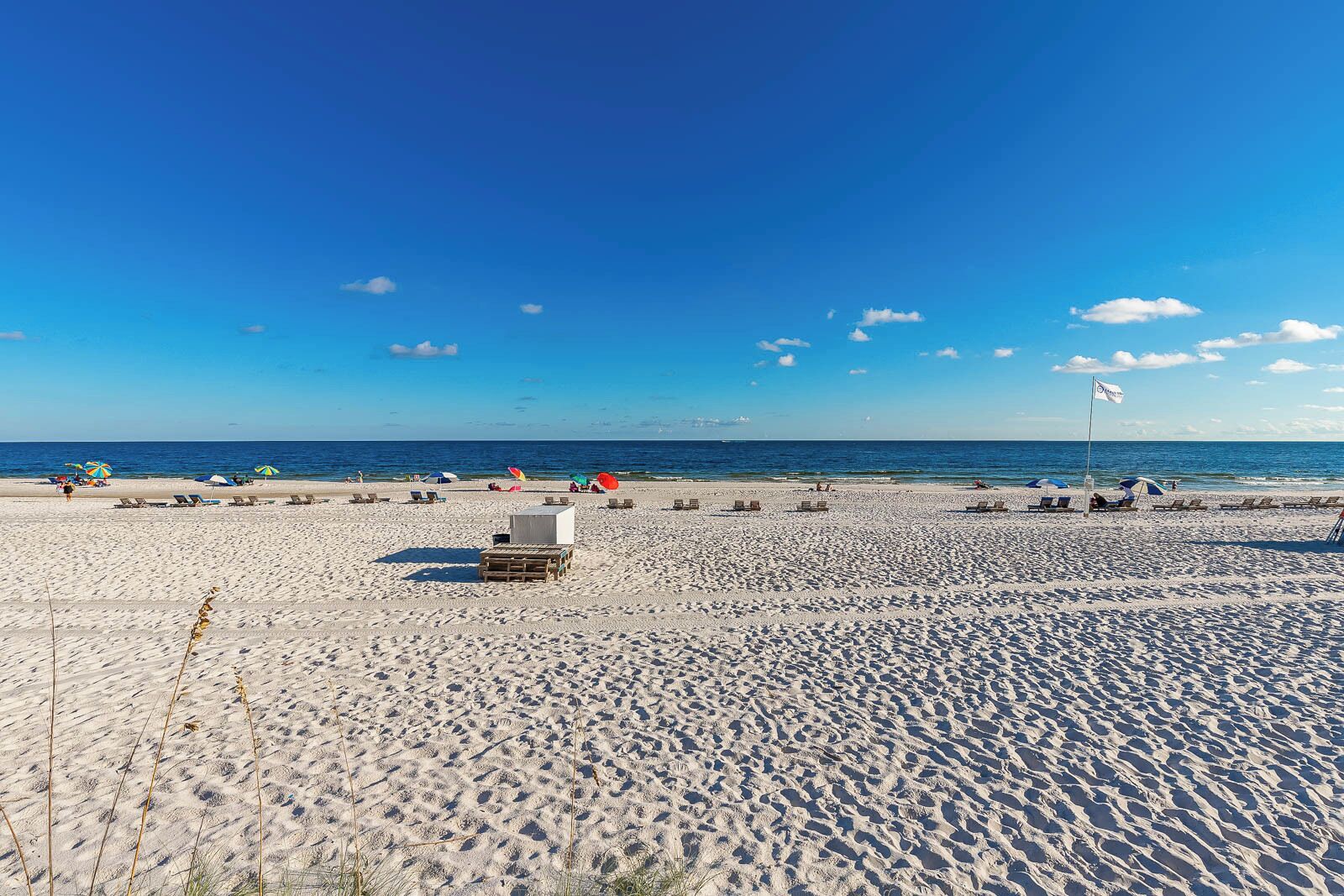 A beach with sun loungers and umbrellas, a flag, and a clear blue sky.